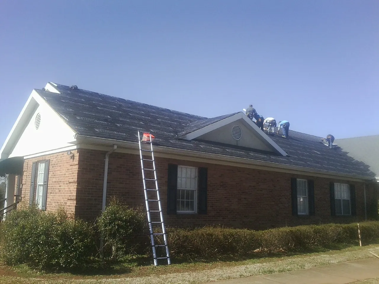 Crew tearing shingles off a brick ranch roof with a ladder set — Metal Roof Repair work by our crew in Racine
