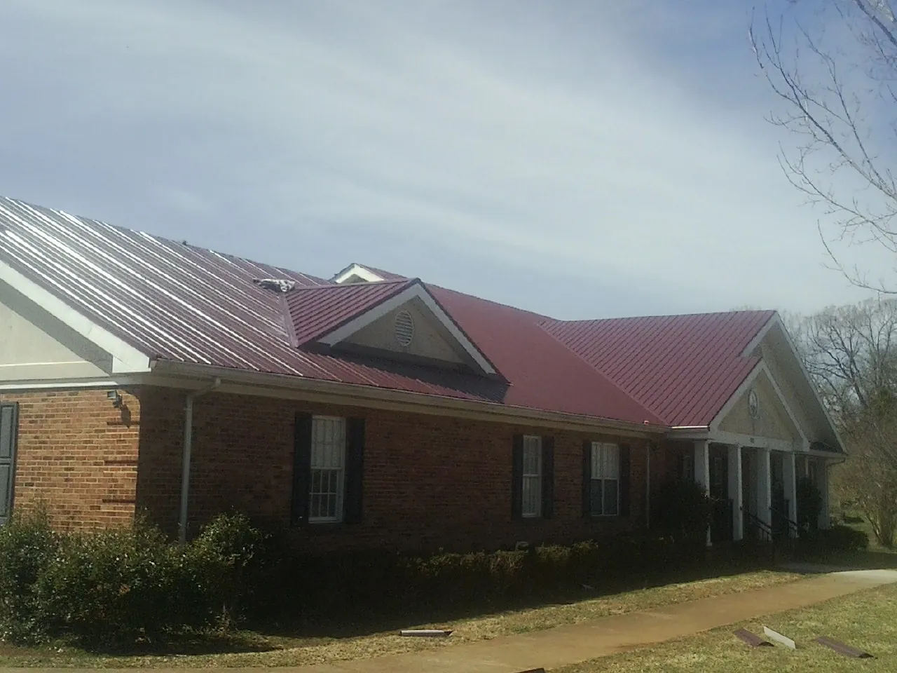 Red metal roof with gabled entries on a long brick building, from a Hail Damage Roof Repair job in Racine