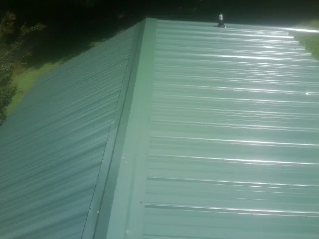 New green metal panels meeting at the ridge of a roof — Flat Roof Repair work by our crew in Racine