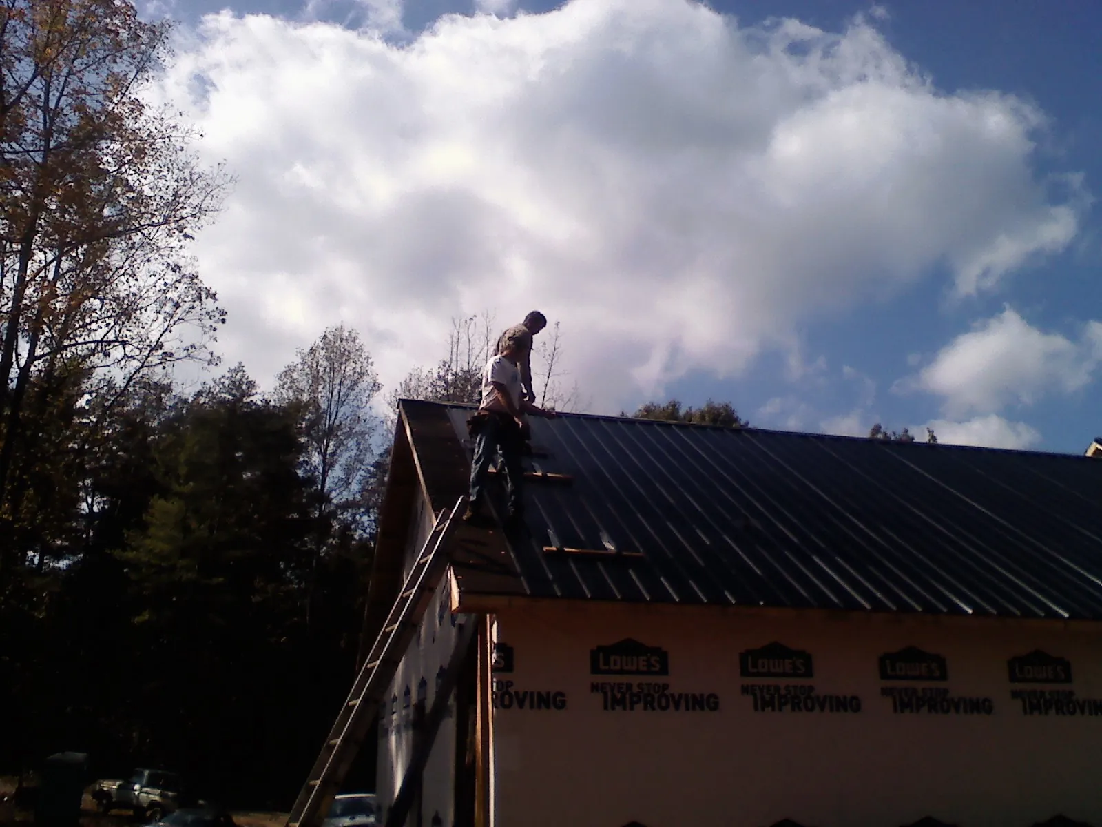 Roofer fastening dark metal panels high against a cloudy sky, from a Roof Inspection job in Racine